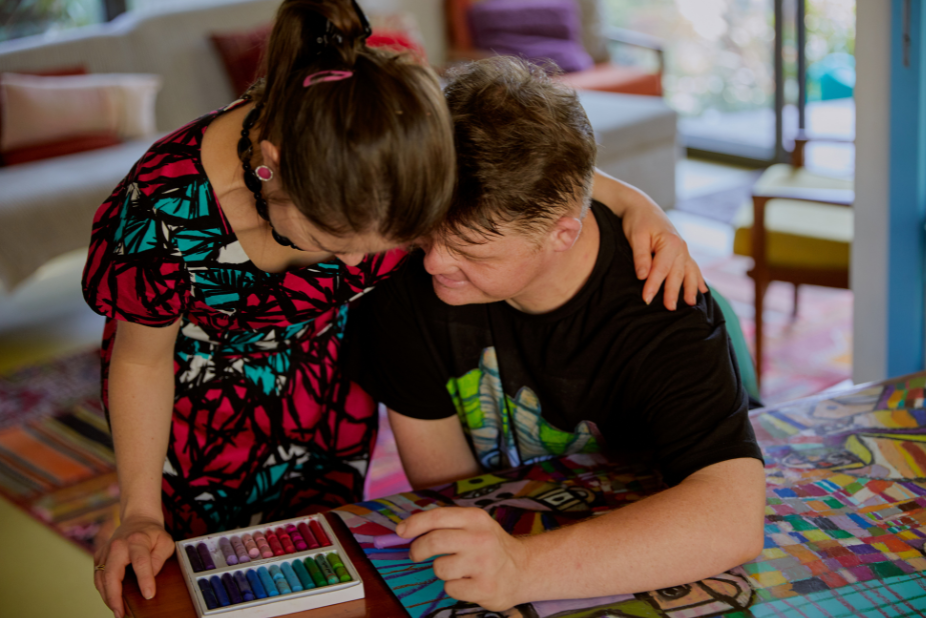 Two people hug over a table of art