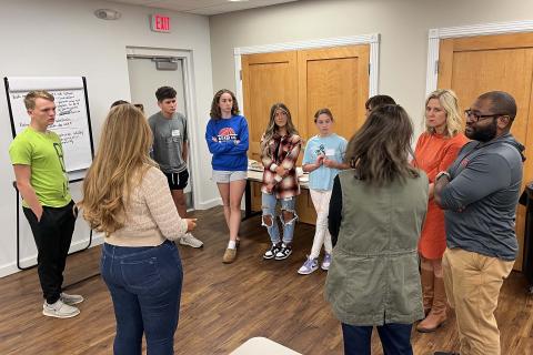 Youth and adults stand in a circle, discussing an issue